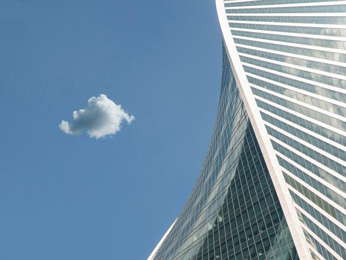 Современная стеклянная башня на фоне голубого неба с одиночным облаком Современная стеклянная башня на фоне голубого неба с одиночным облаком